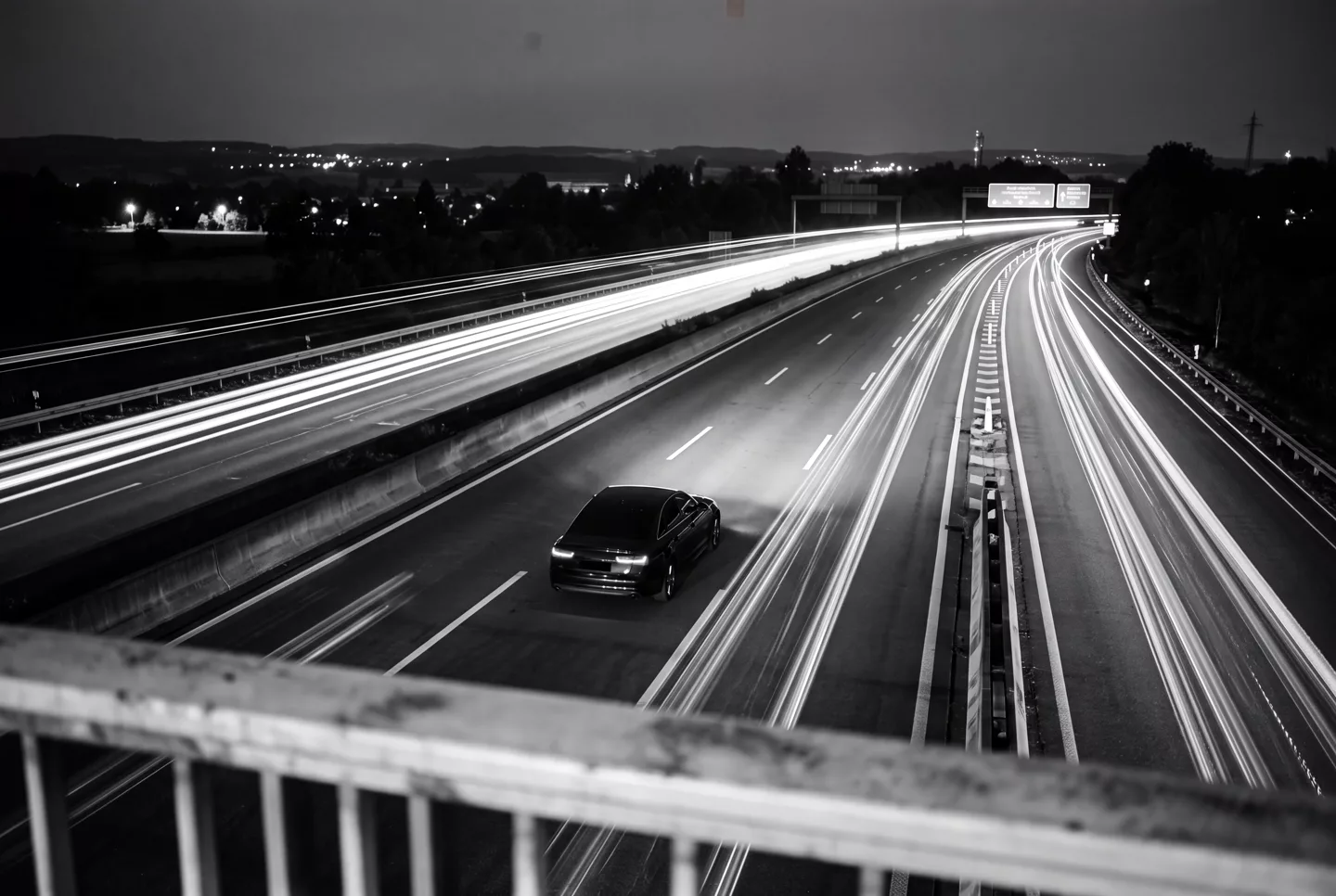 Inszenierte Schwarzweiß-Langzeitbelichtung: Limousine bei Nacht auf der Autobahn, Lichtspuren im Hintergrund